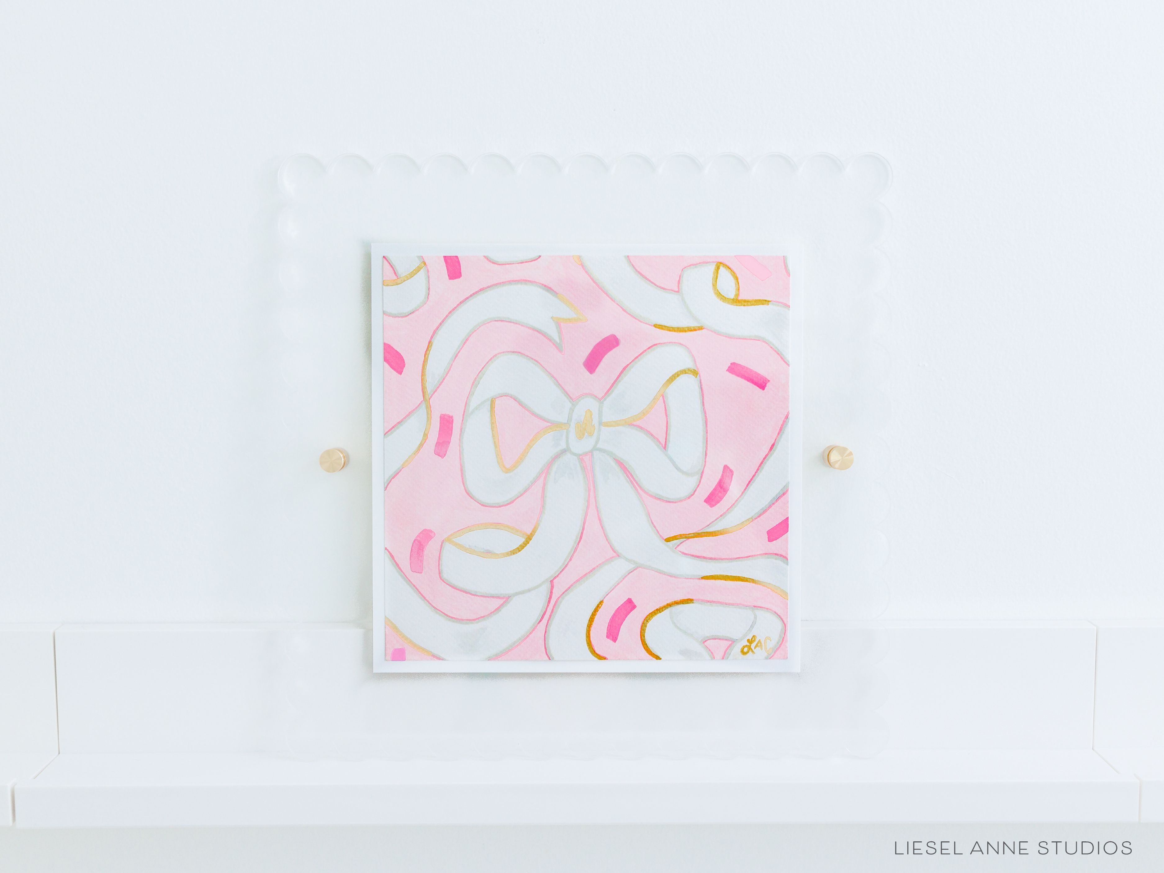 Golden Bows Pink & White 05 [Original Artwork + Clear Scalloped Frame]-Original artwork measures 8"x8" | Hand-Painted with gouache on cold press watercolor paper | Matted and framed in an acrylic scalloped frame sized 12"x12" | Hanging hardware and acrylic clear stand included | Features our signature Golden Bows design with a light pink base, white bows and shimmery gold accents | Initialed in gold by Liesel Anne (the artist) on the front and signed and dated on the back-The Singing Little Bird