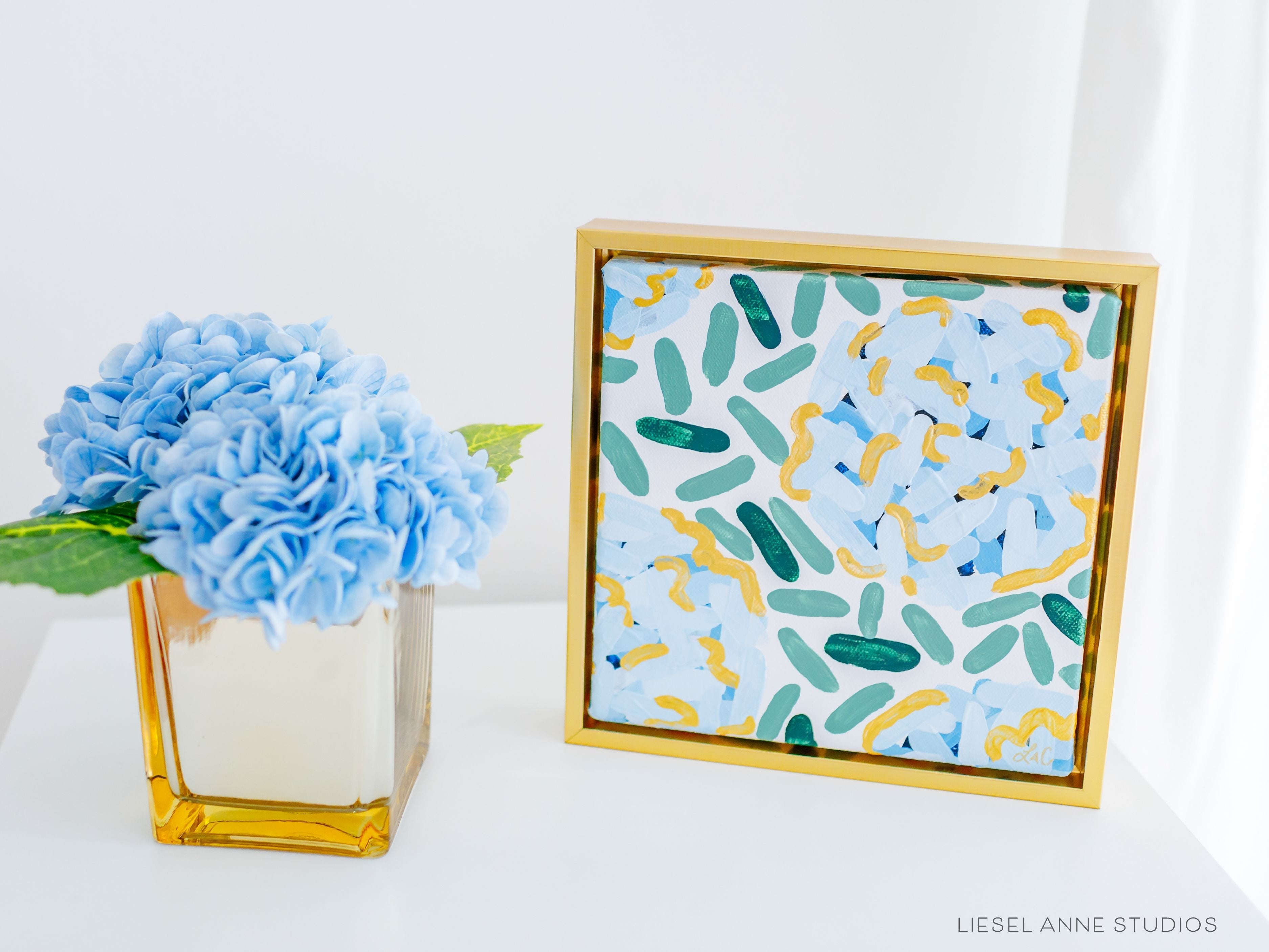 Golden Hydrangea | White & Blue XXVI-Original artwork measures 5"x5" | Framed in gold wood floater frame | Hand-Painted with gouache on stretched canvas | Features our signature Golden Hydrangea design with a white base, blue hydrangeas and shimmery gold accents | Initialed in gold by the Liesel Anne (the artist) on the front and signed and dated on the back-The Singing Little Bird