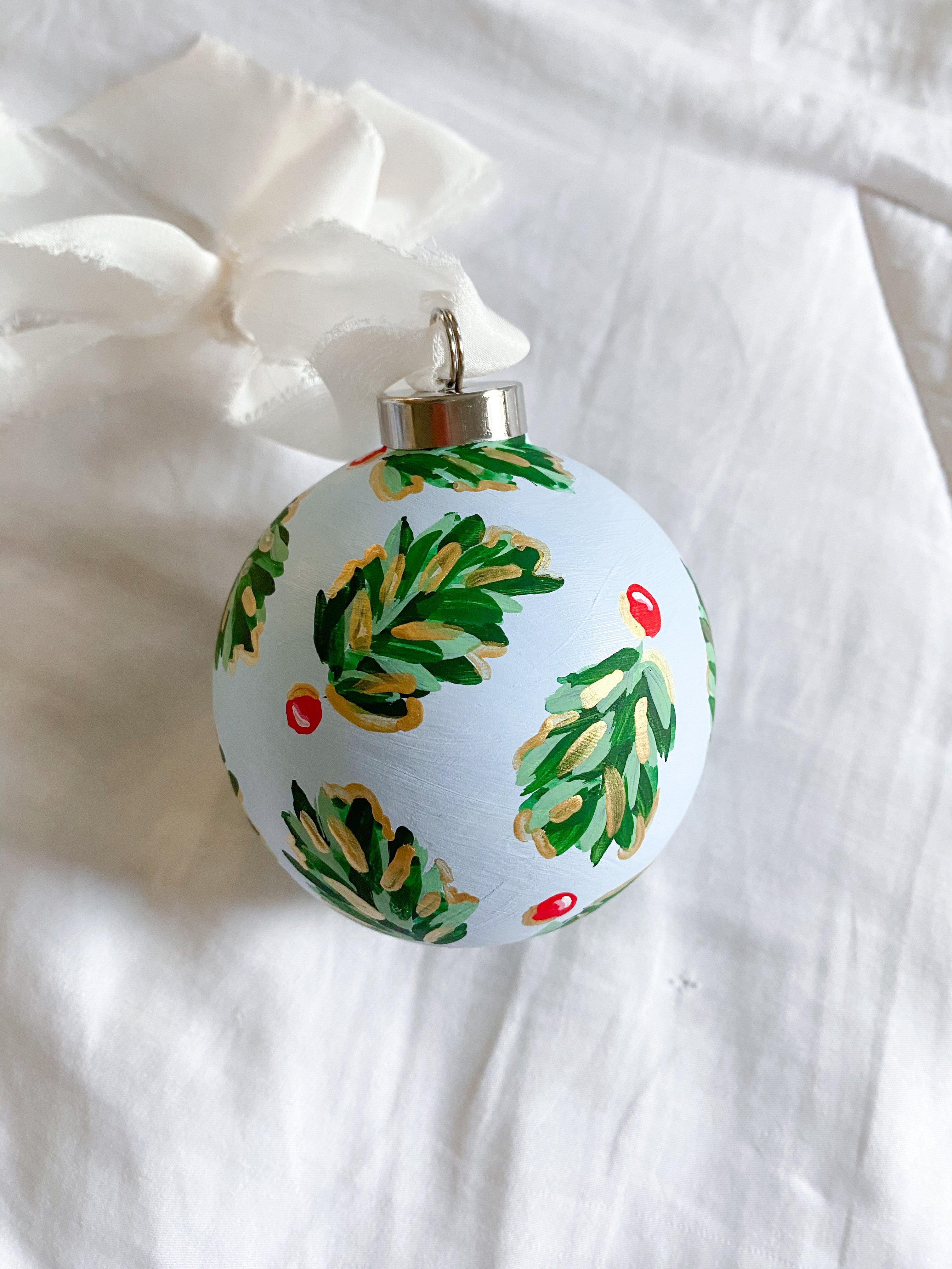 Icy Blue Golden Holly Bauble-Ceramic Hand-Painted Keepsake Ornament | Measuring 3" x 3" | Features the Golden Holly design with a light blue base and shimmery gold accents | Coated with a protective matte finish that will keep it protected and shimmering year after year | Your color choice of silk crepe ribbon with a frayed edge for hanging | Each bauble is slightly different with potential small imperfections due to the hand-painted nature, making each one special and unique!-The Singing Little Bird