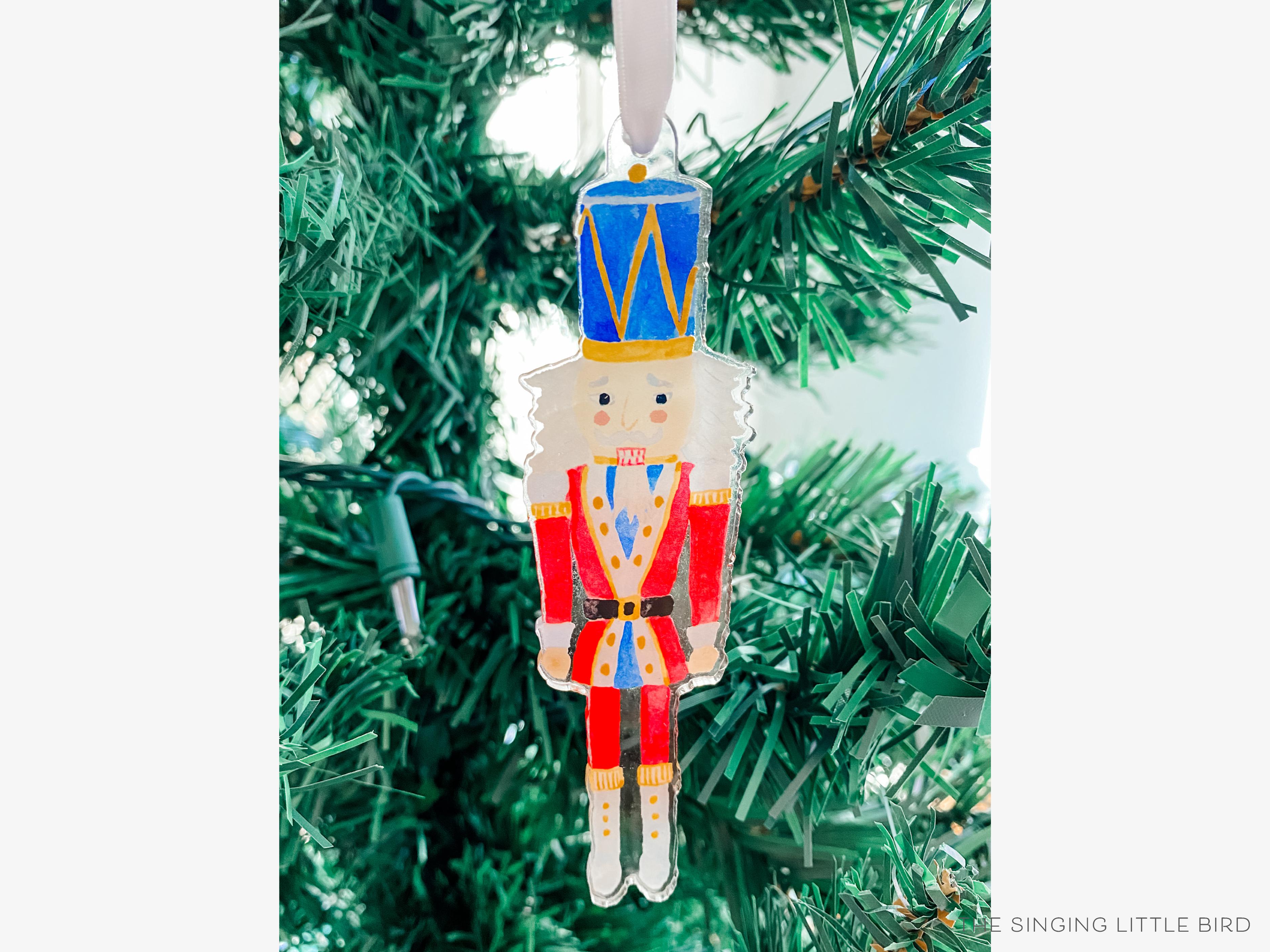 Nutcracker Acrylic Ornament-These acrylic ornaments feature our hand-painted watercolor Nutcracker. They include a white silk ribbon and measure approximately 4" on its longest side, making a great addition to your Christmas tree or gift for the Nutcracker lover in your life.-The Singing Little Bird