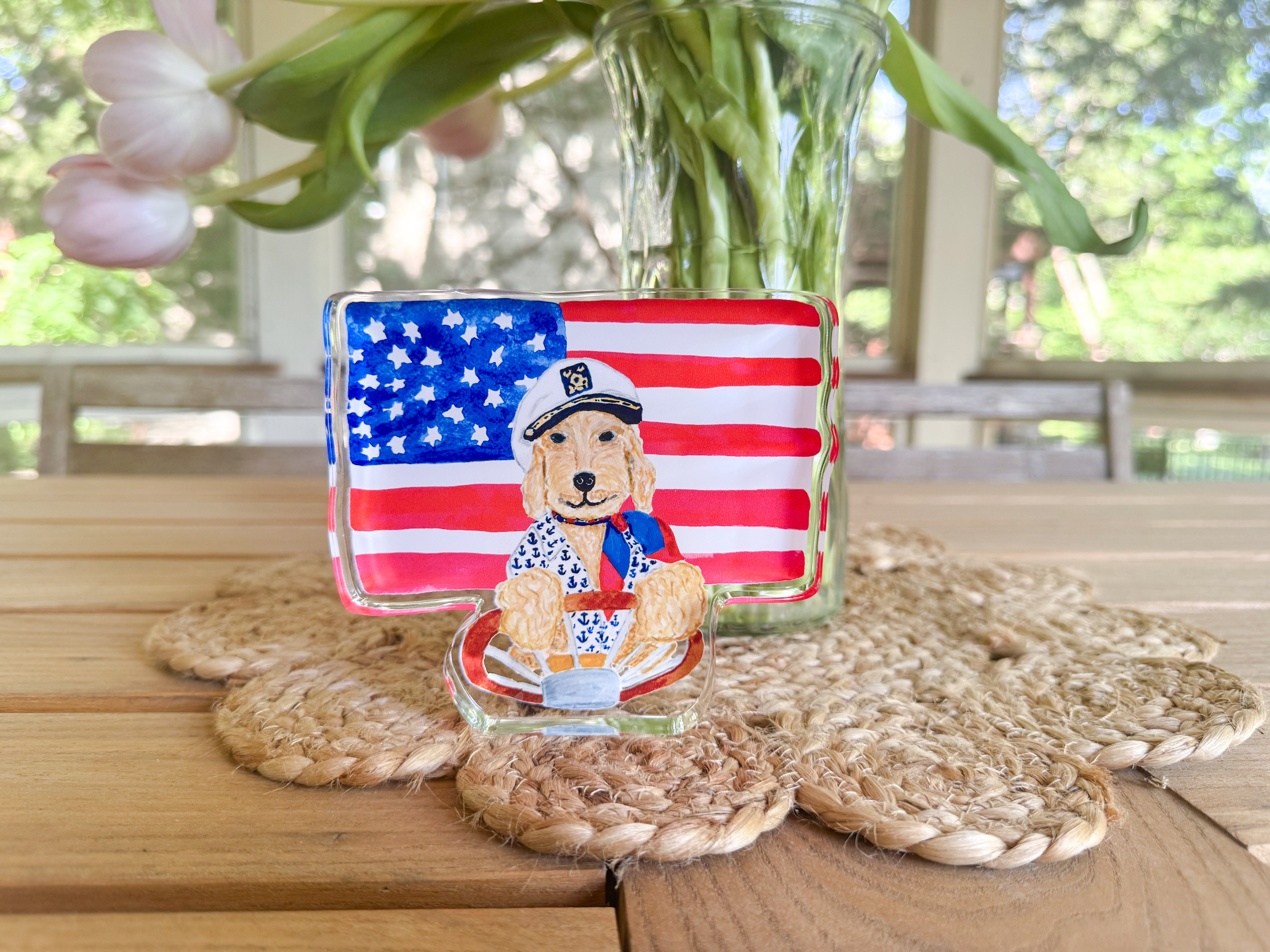a wooden table with a glass vase containing green beans, a glass picture frame with a dog wearing a sailor hat, and a woven placemat.