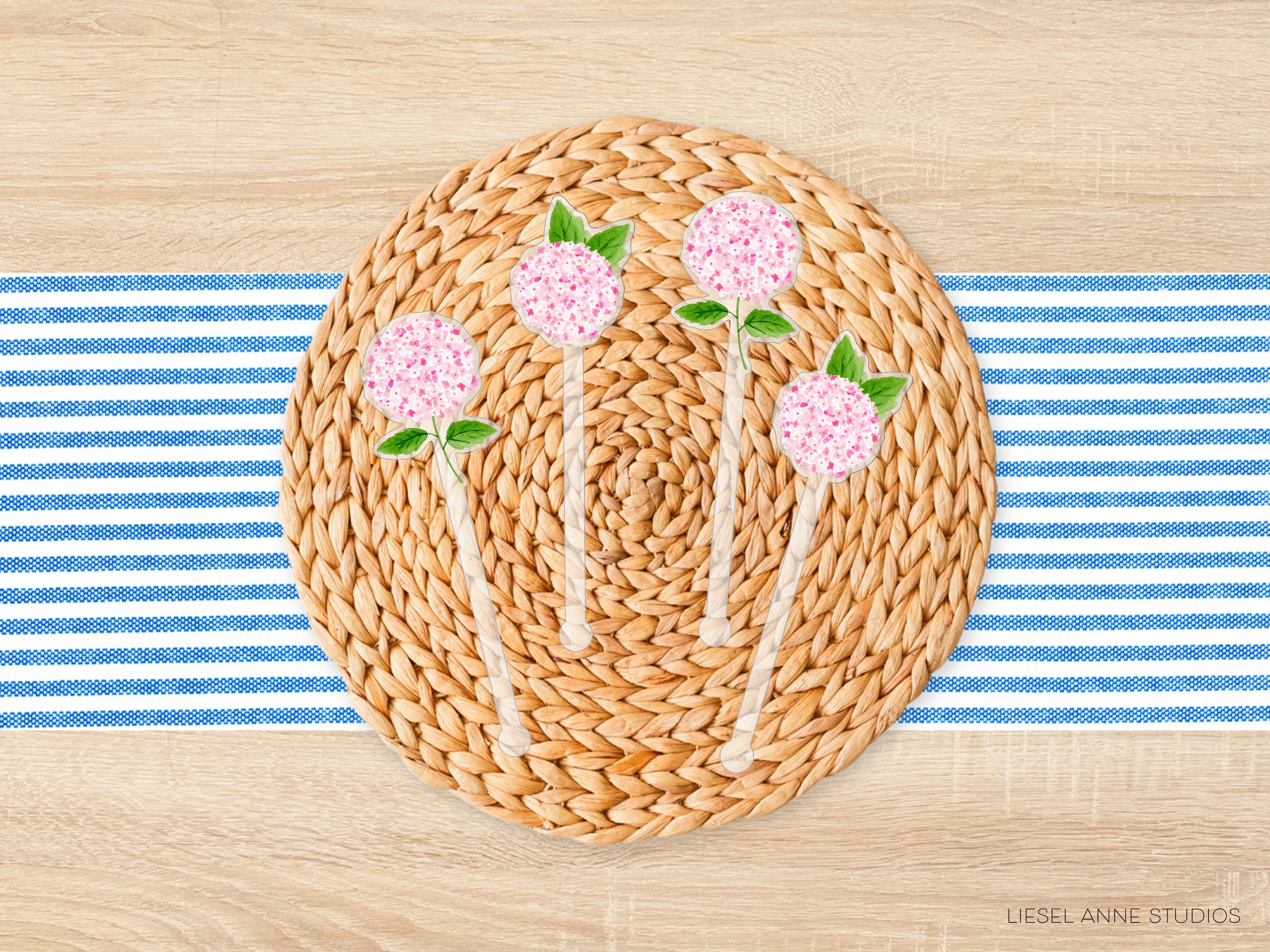 A woven placemat with a blue and white striped tablecloth, featuring four pink flowers with green leaves on a round wicker base.