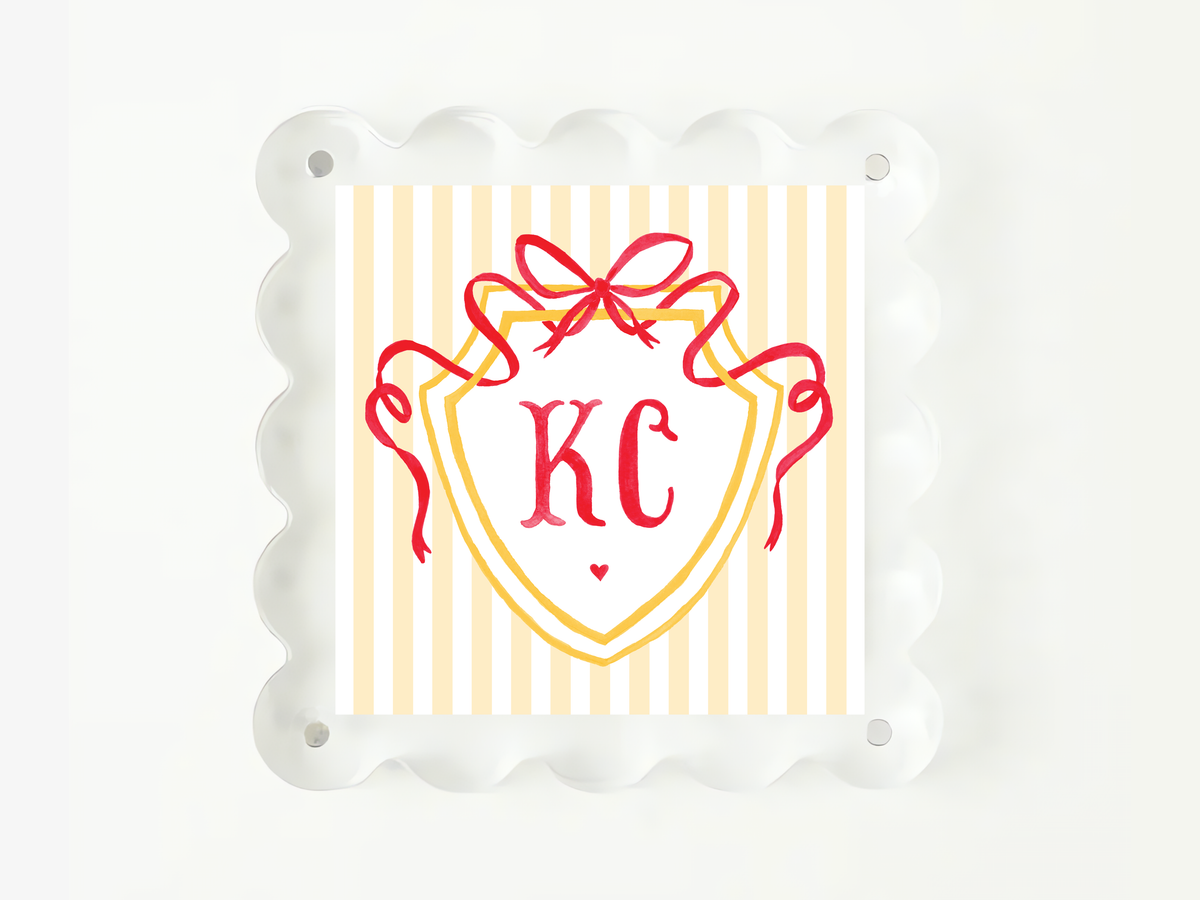 A square image with a decorative border, featuring a shield-shaped design with a red ribbon and the initials "KC" prominently displayed in the center.