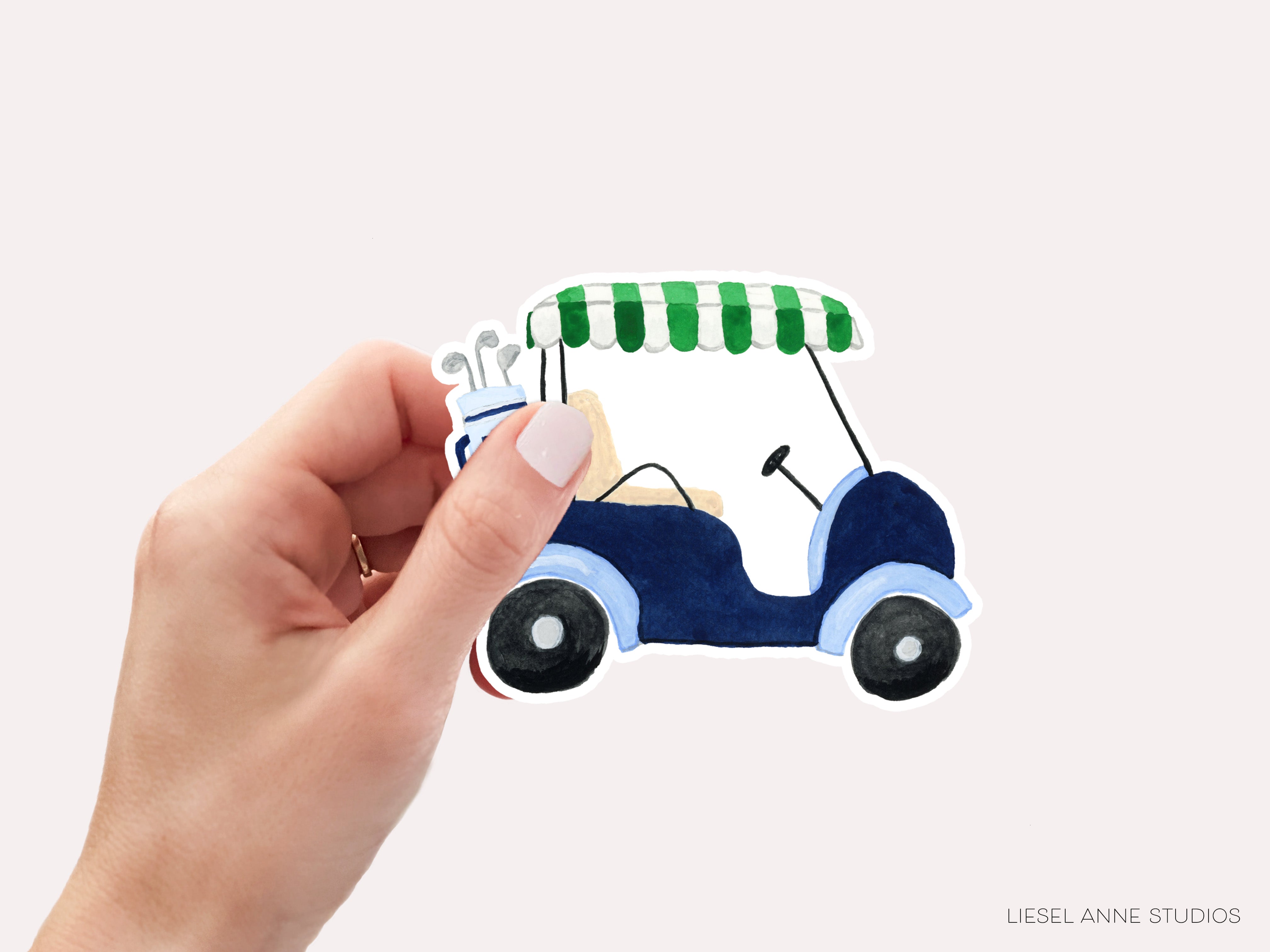 A hand holding a sticker of a golf cart against a light background.