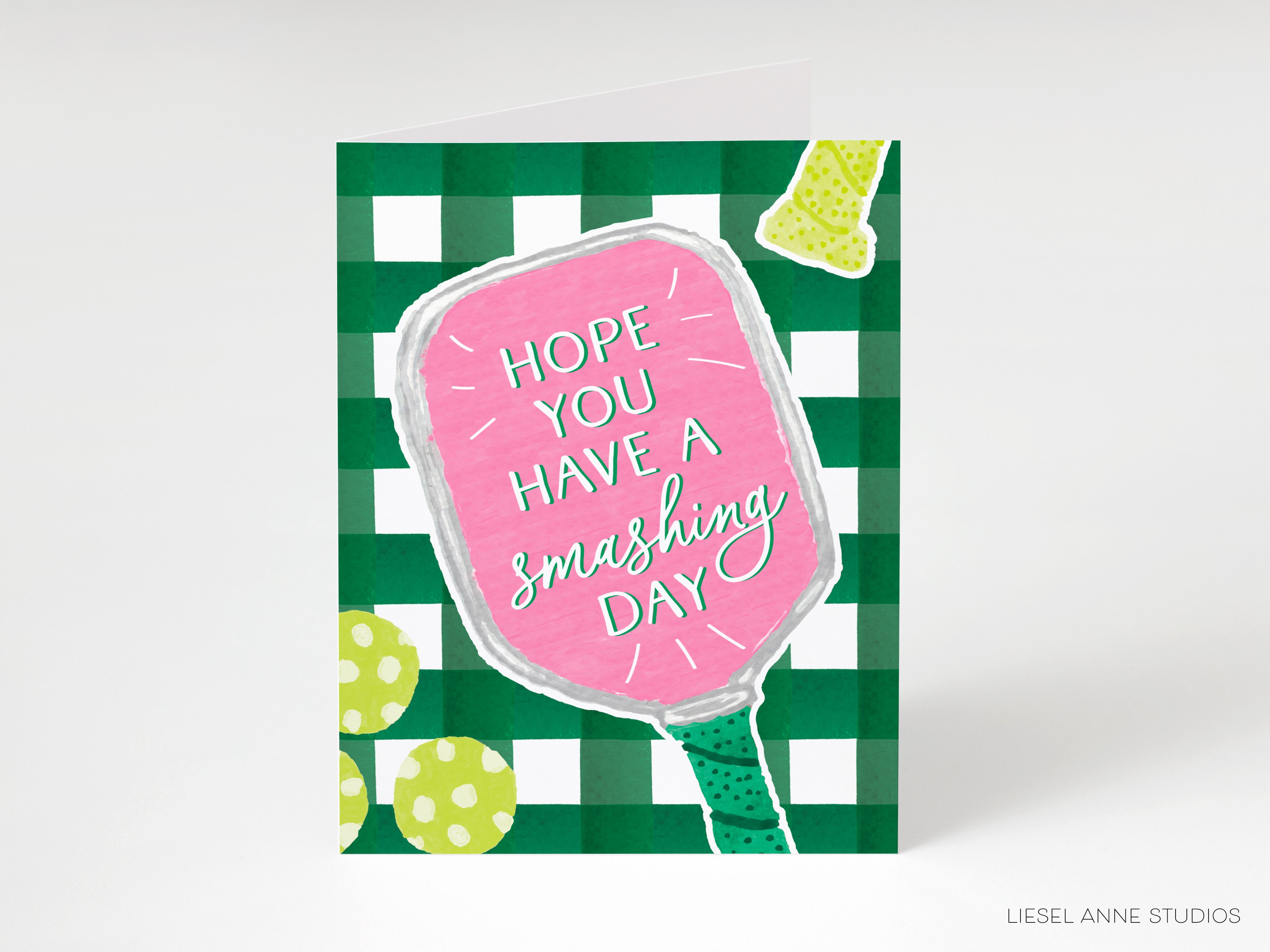 The image is a greeting card with a pink paddle and a green and white checkered background. The text on the card reads "HOPE YOU HAVE A SMASHING DAY".