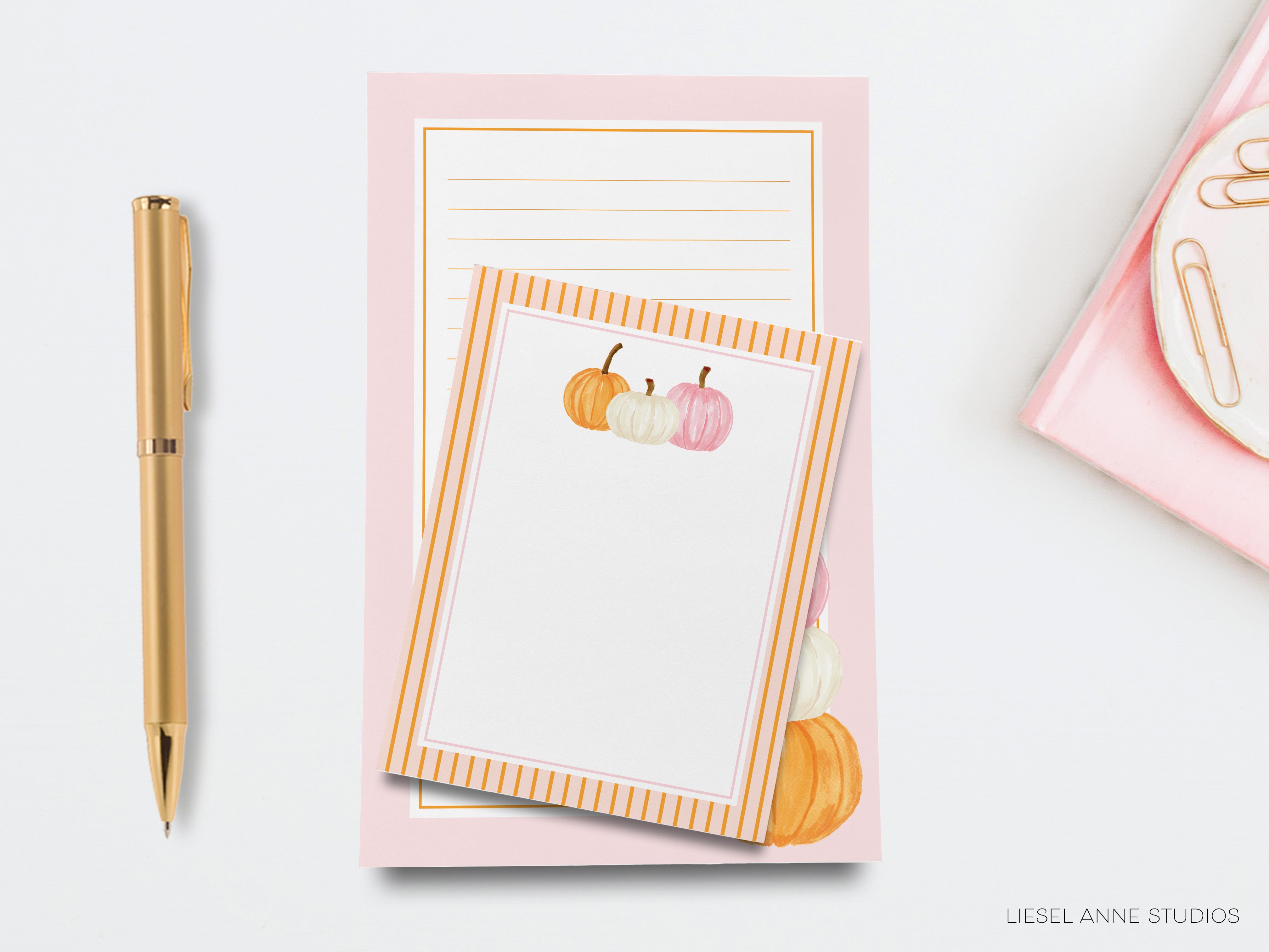 a pink notepad with a gold pen and a gold stapler on a white background.