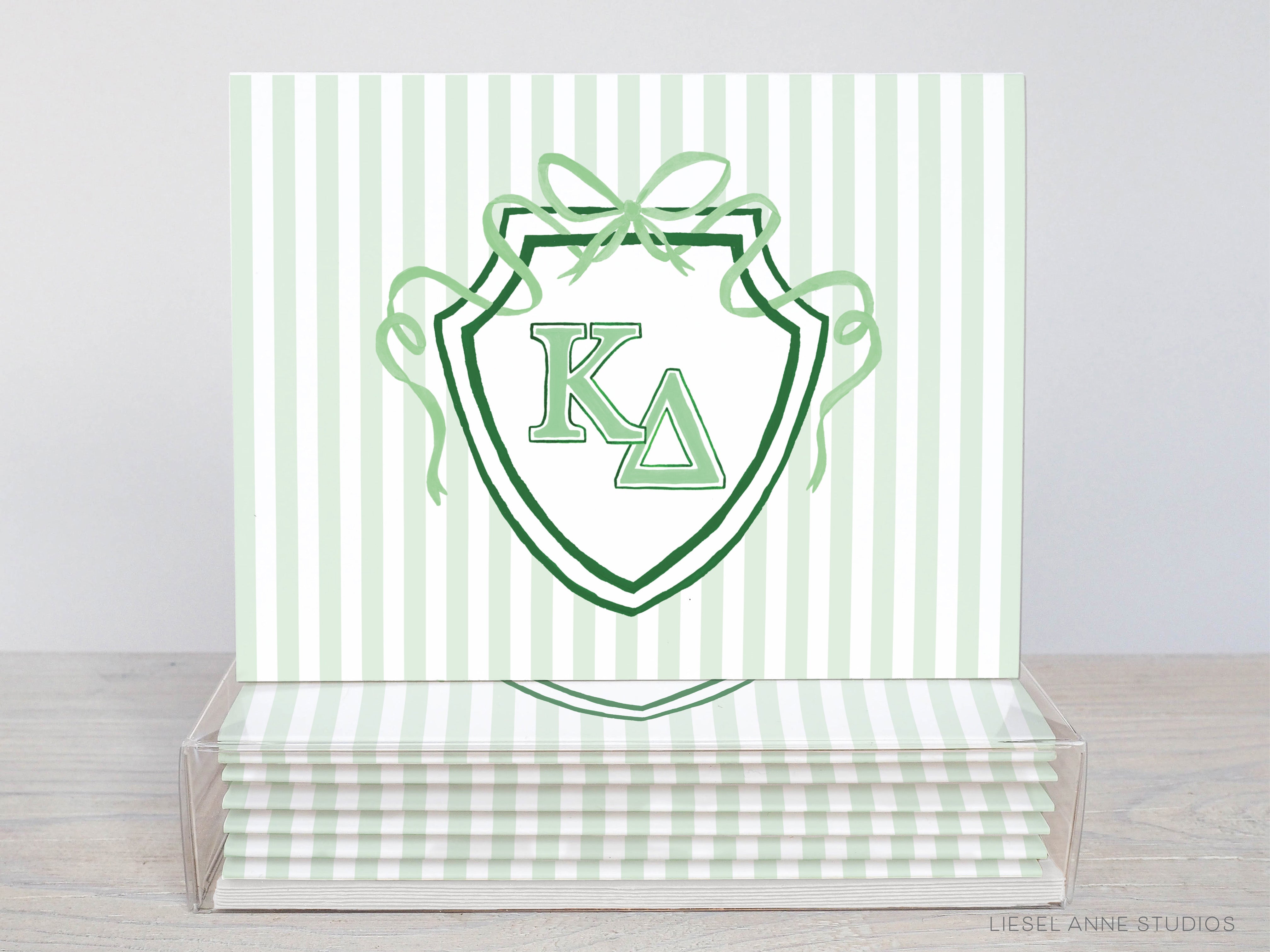 A stack of green and white striped greeting cards with a shield-shaped logo featuring the letters 'K' and 'Δ' in the center.