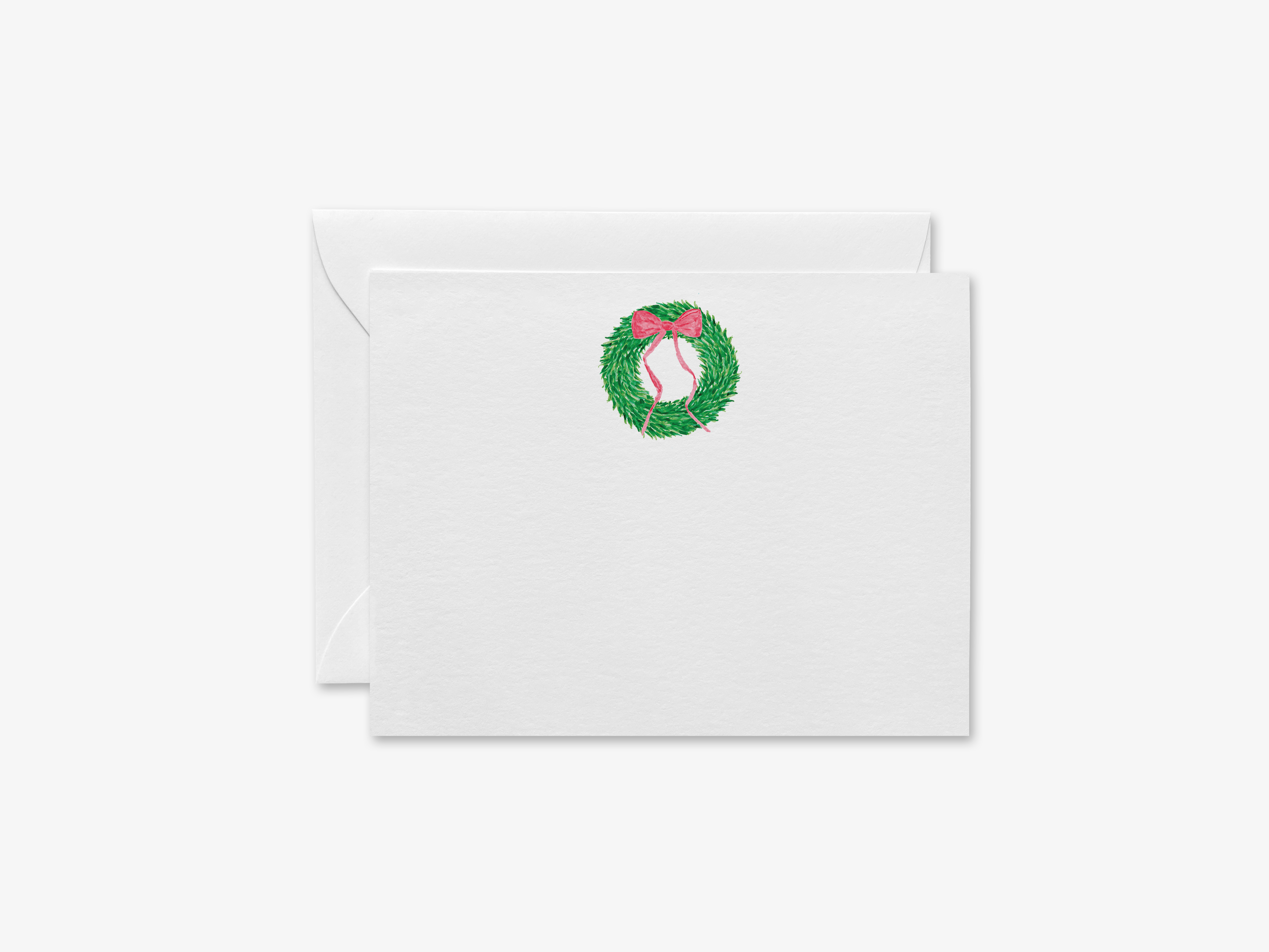 A white envelope with a green wreath and a red bow on top, along with a white card.
