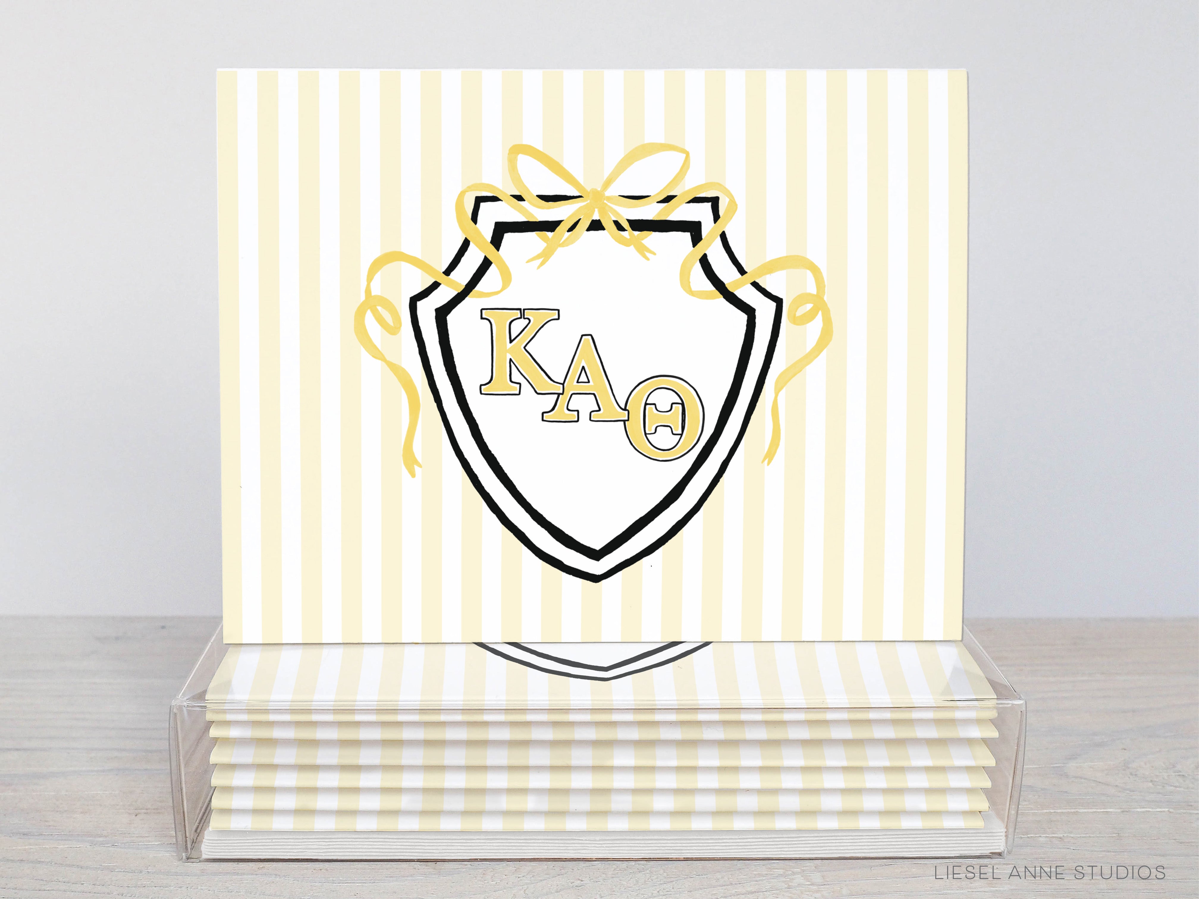 A stack of white and yellow striped greeting cards with a shield-shaped design featuring the letters "KA" and a ribbon.