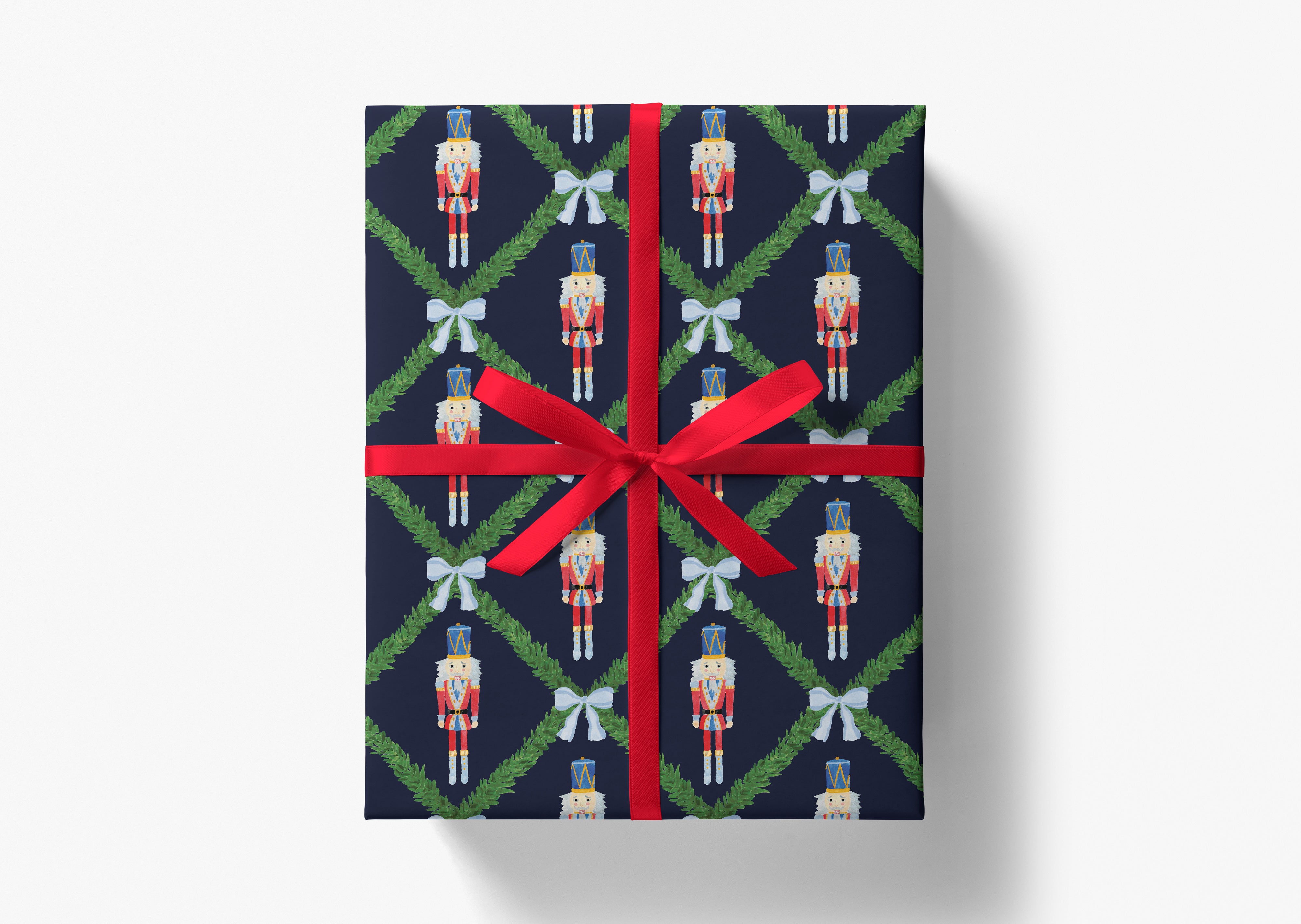 A gift box wrapped in a navy blue wrapping paper with a red ribbon. The wrapping paper has a repeating pattern of nutcracker figures and green leaves.