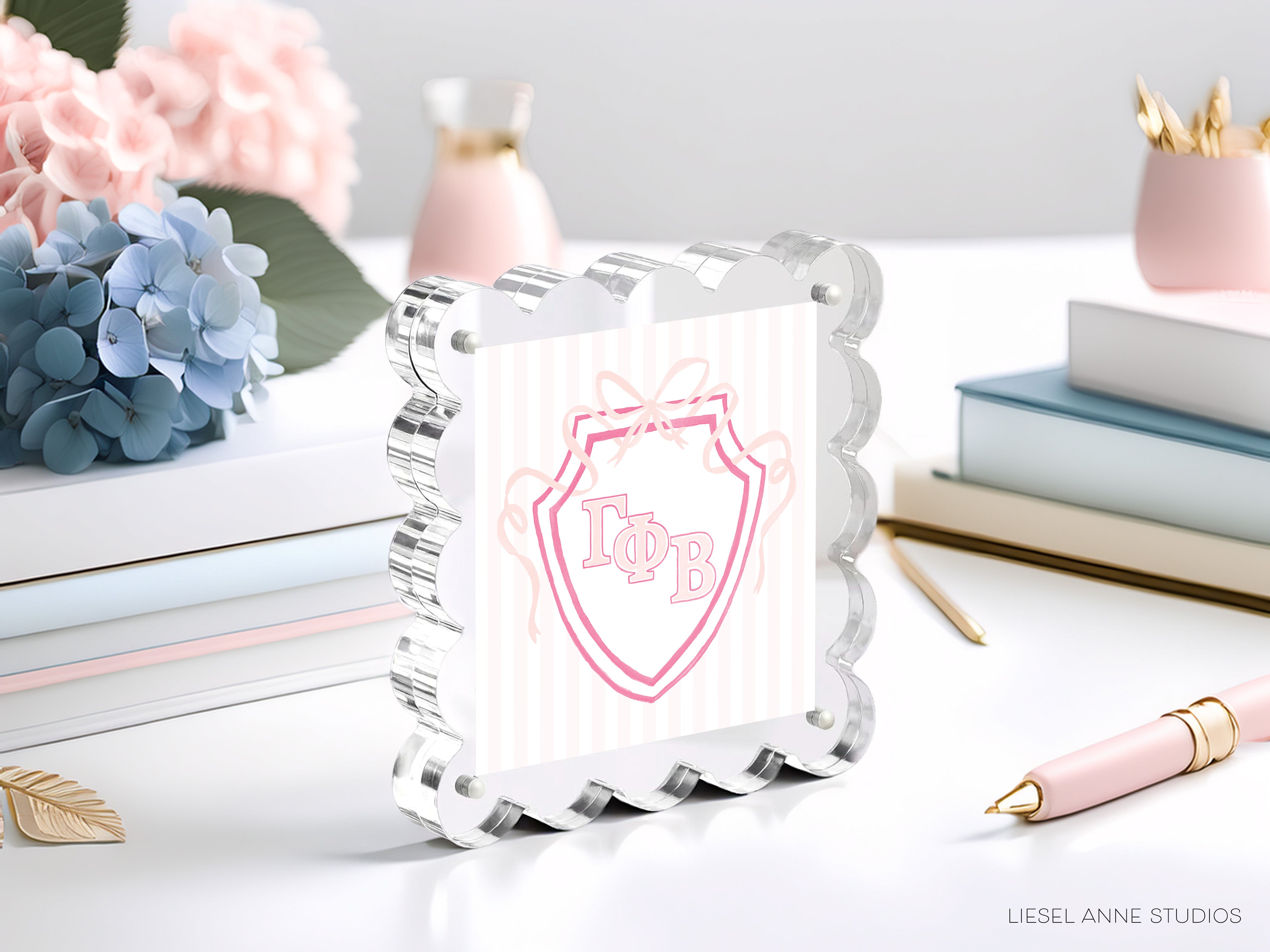 A clear glass frame with a pink and white shield design, surrounded by various decorative items such as flowers, books, and a pen on a white surface.