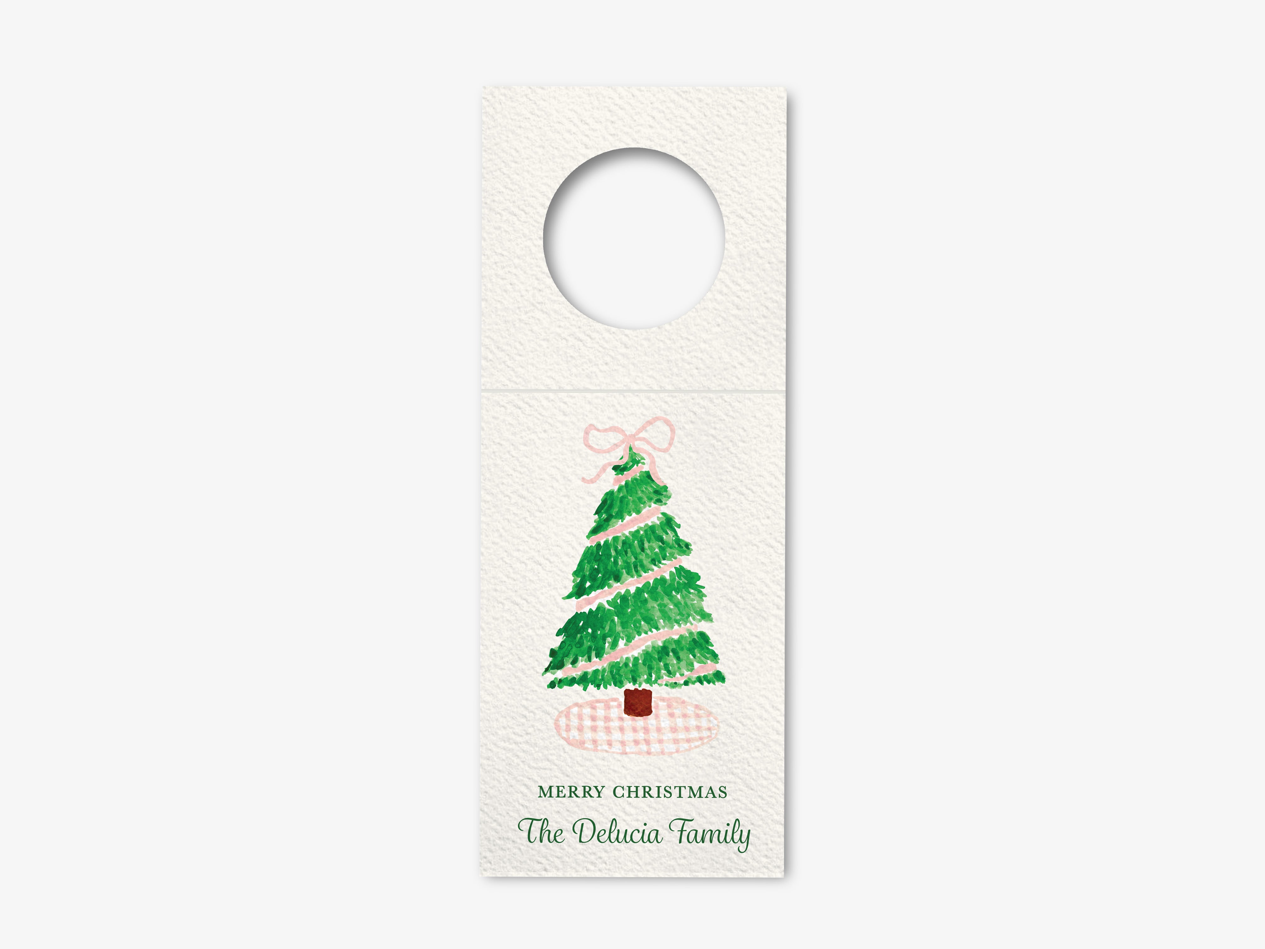 A white Christmas tree decoration with a pink bow, accompanied by the text "Merry Christmas The Delicia Family".