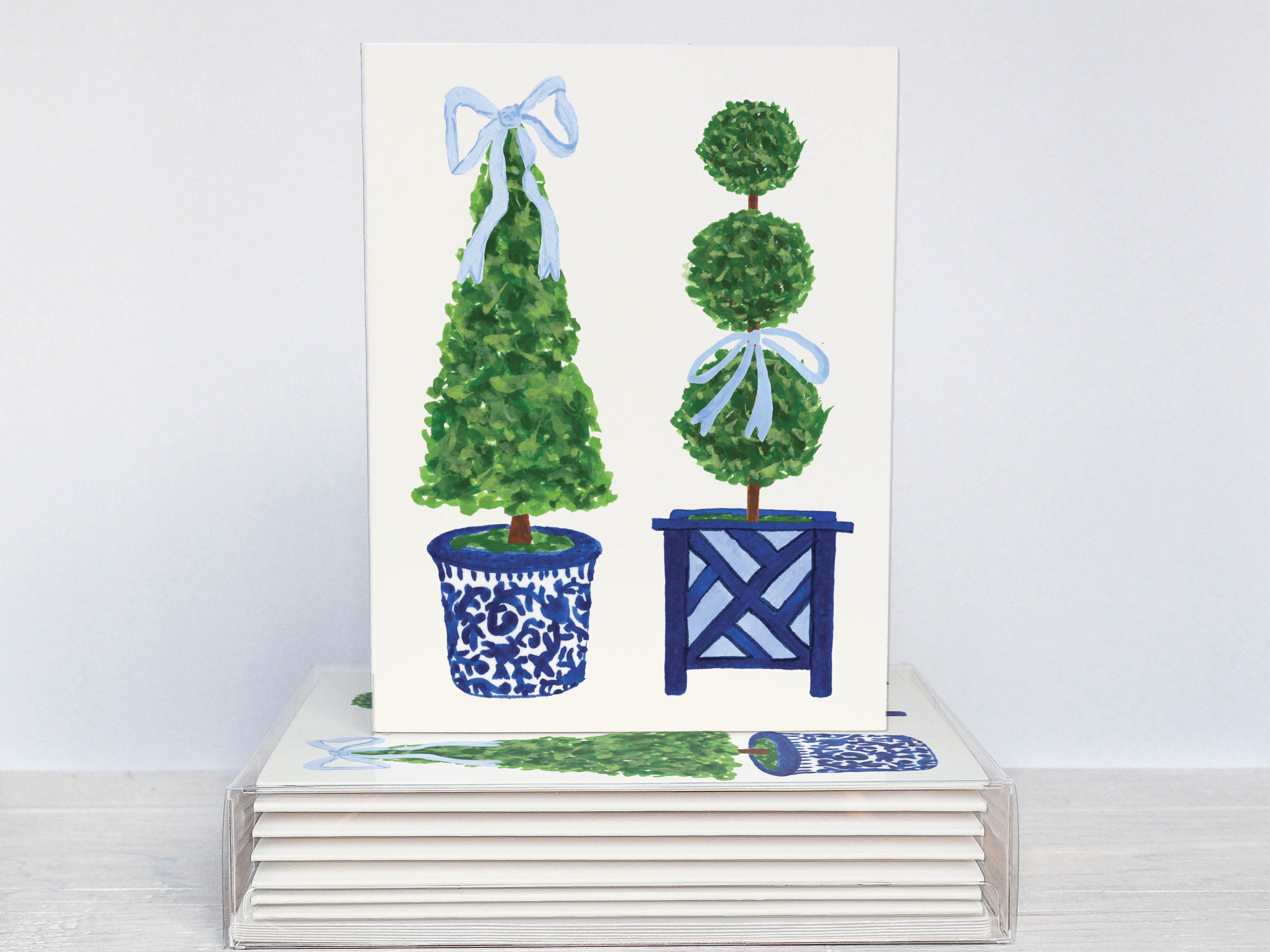 A white card with illustrations of two topiary trees in blue and white vases, placed on a stack of similar cards.