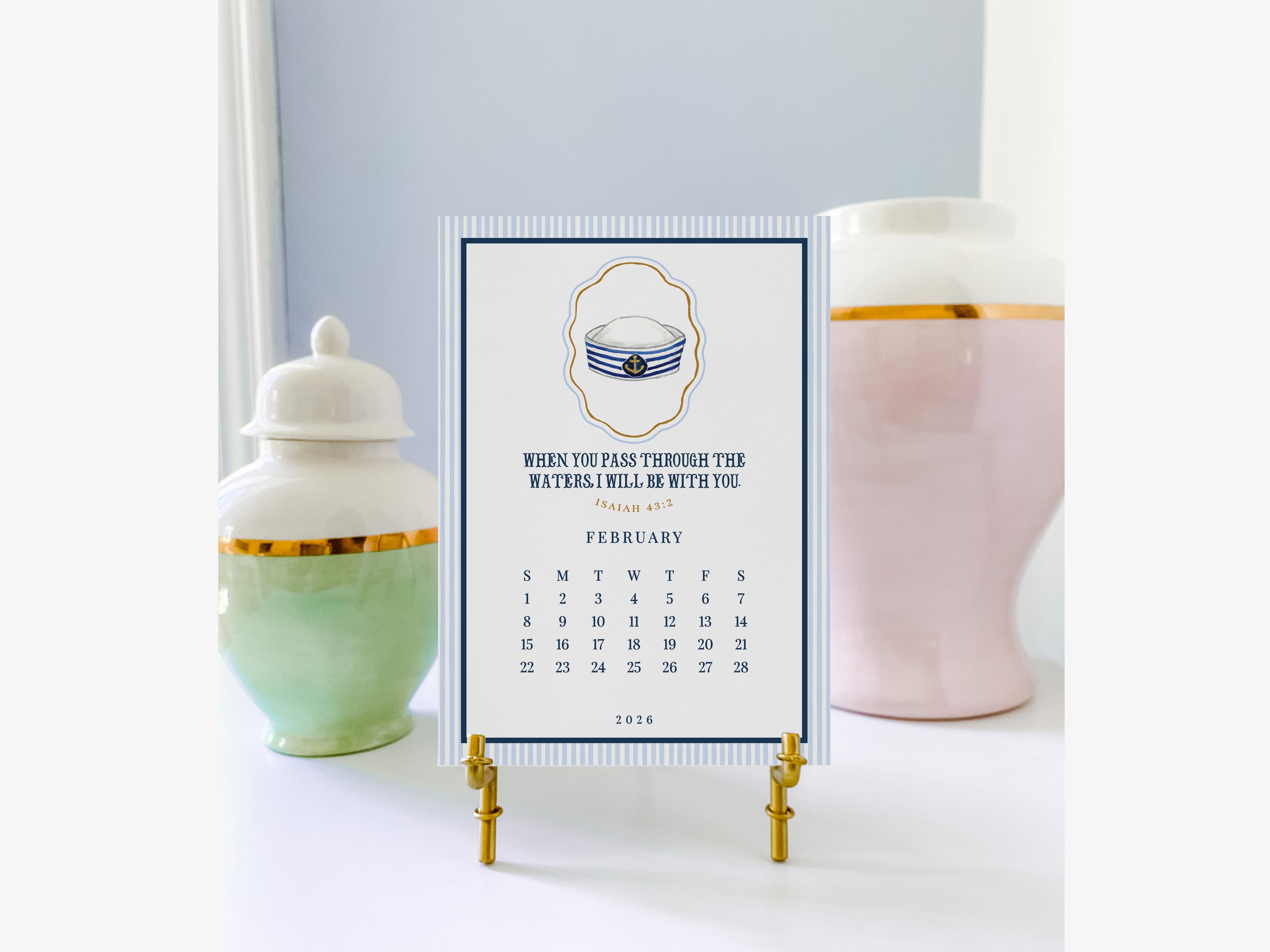 a calendar on a stand with a navy blue and white design, placed between two decorative vases.