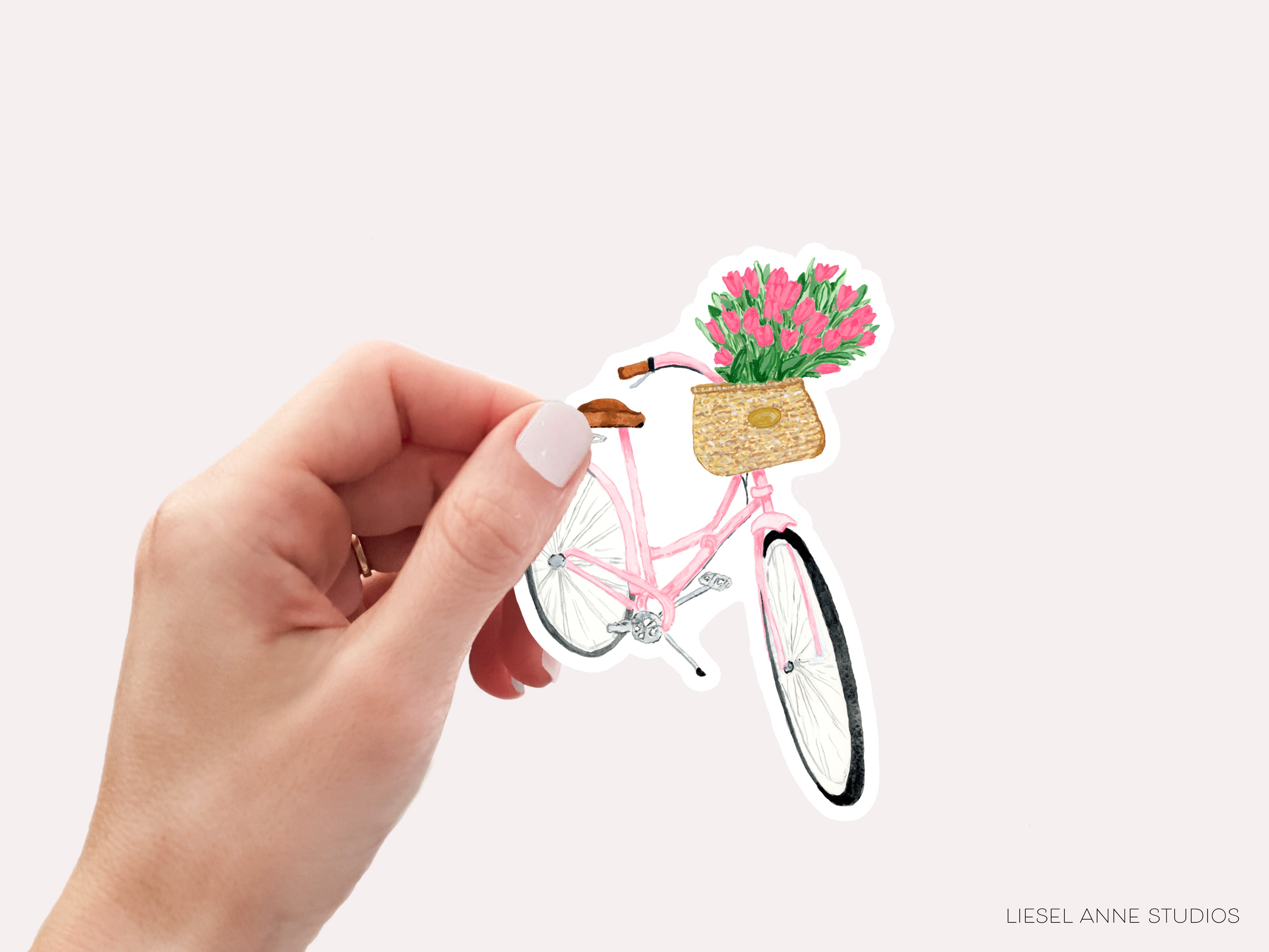A hand holding a sticker depicting a pink bicycle with a basket of flowers.