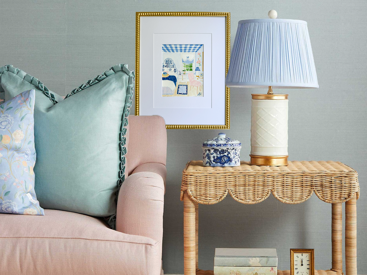 a cozy living room with a pink sofa, a wicker side table, and a blue and white lamp with a white shade. The room has a gray wall and a framed picture hanging on it.