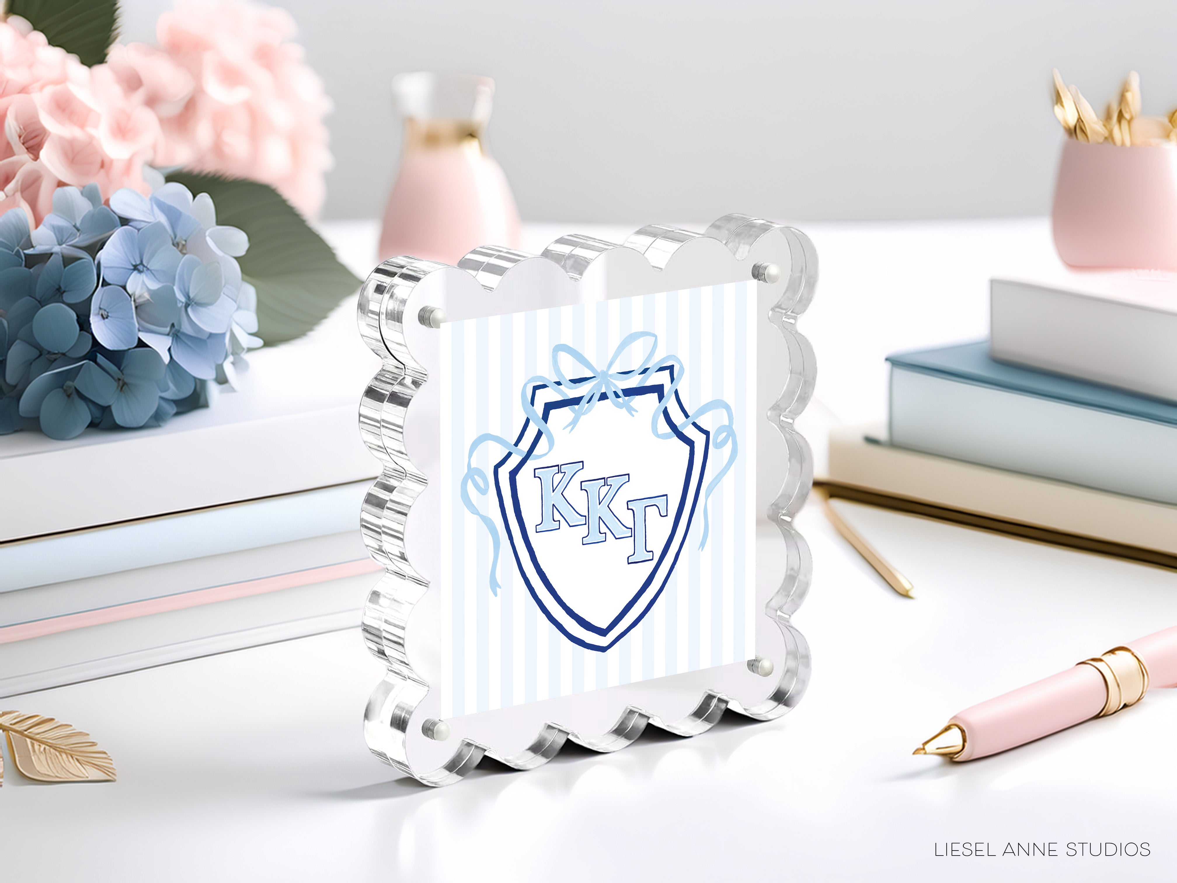 a clear glass picture frame with a blue and white shield design, surrounded by various decorative items such as flowers, books, and a pen on a white surface.