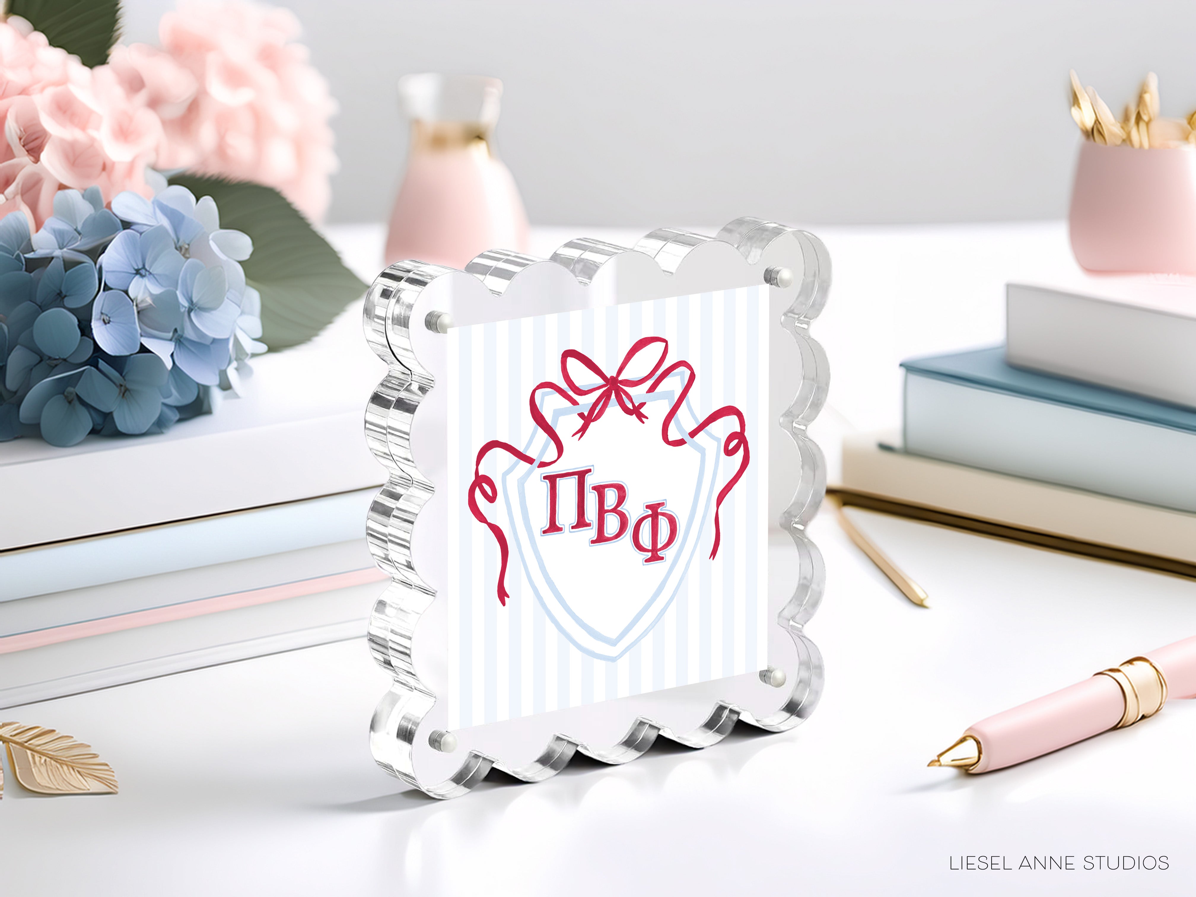a clear glass frame with a decorative border, displaying a red ribbon design and the Greek letters "ΦΑΓΟ" (ΦΑΓΟ). The frame is placed on a table surrounded by various objects, including a stack of books, a vase, and a pink flower.
