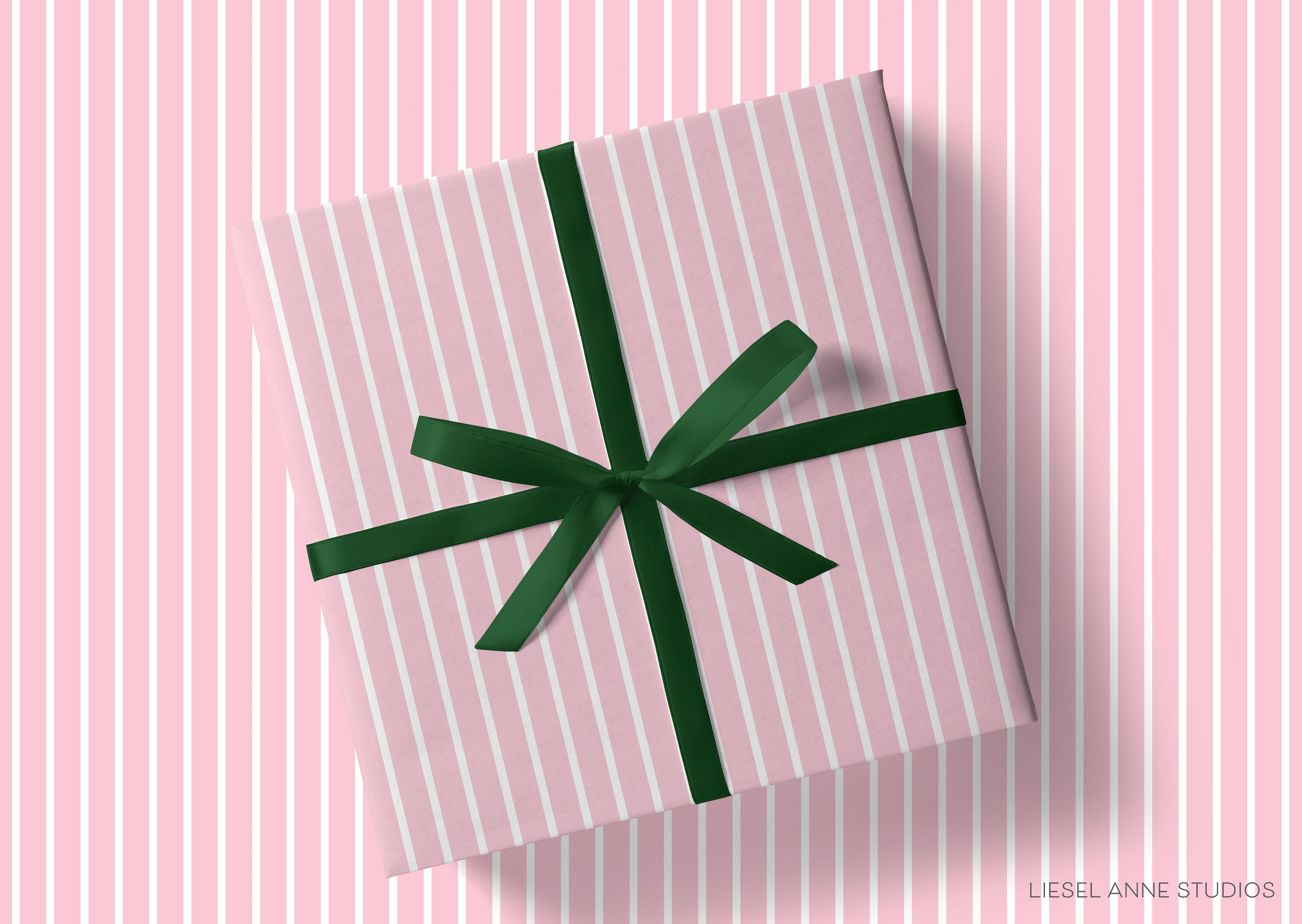 A pink gift box with a green ribbon tied around it, placed on a pink striped background.