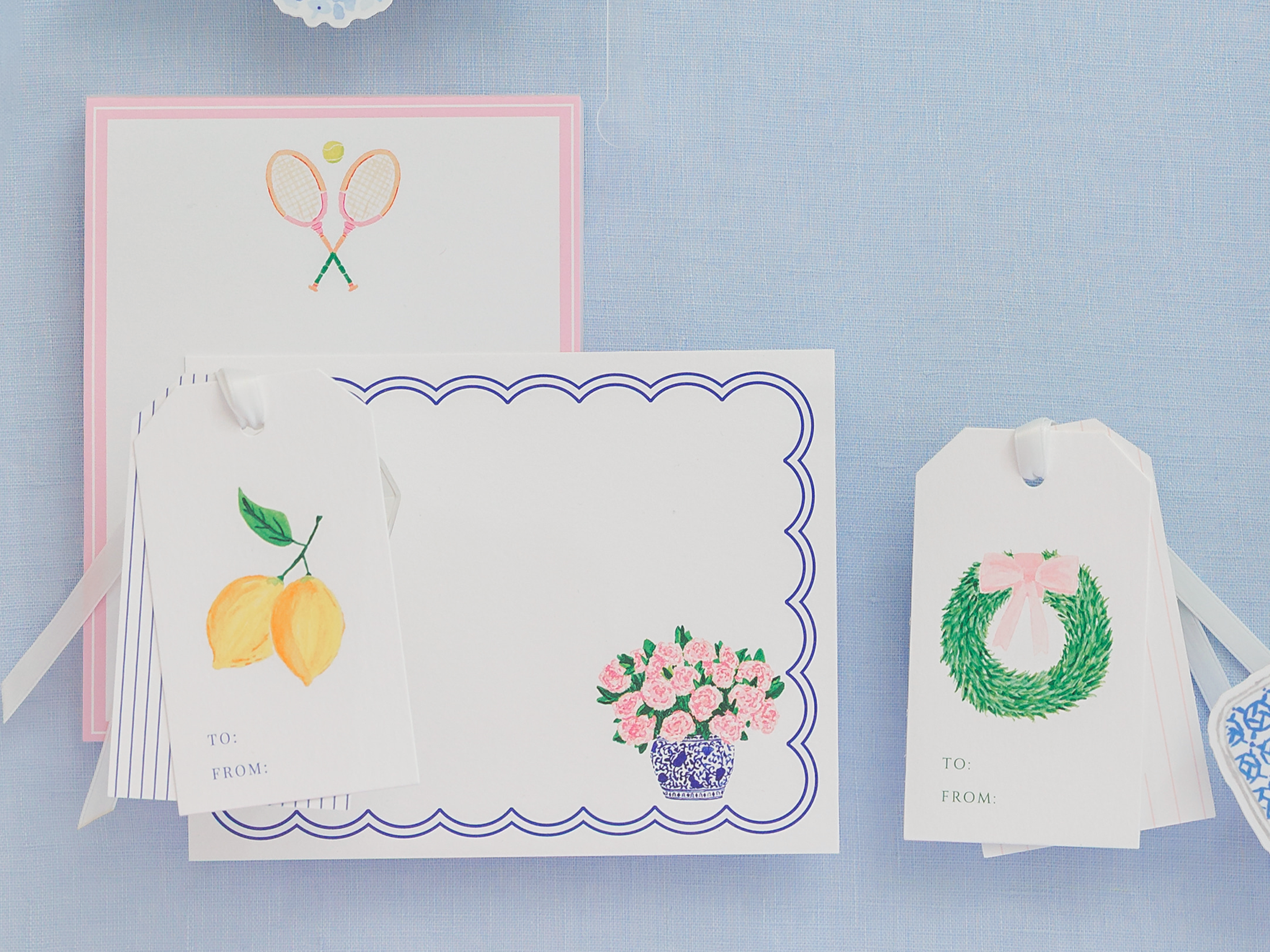 a collection of three items, including a pink envelope with tennis rackets, a white card with a vase of flowers, and two white tags with illustrations of lemons and a wreath.