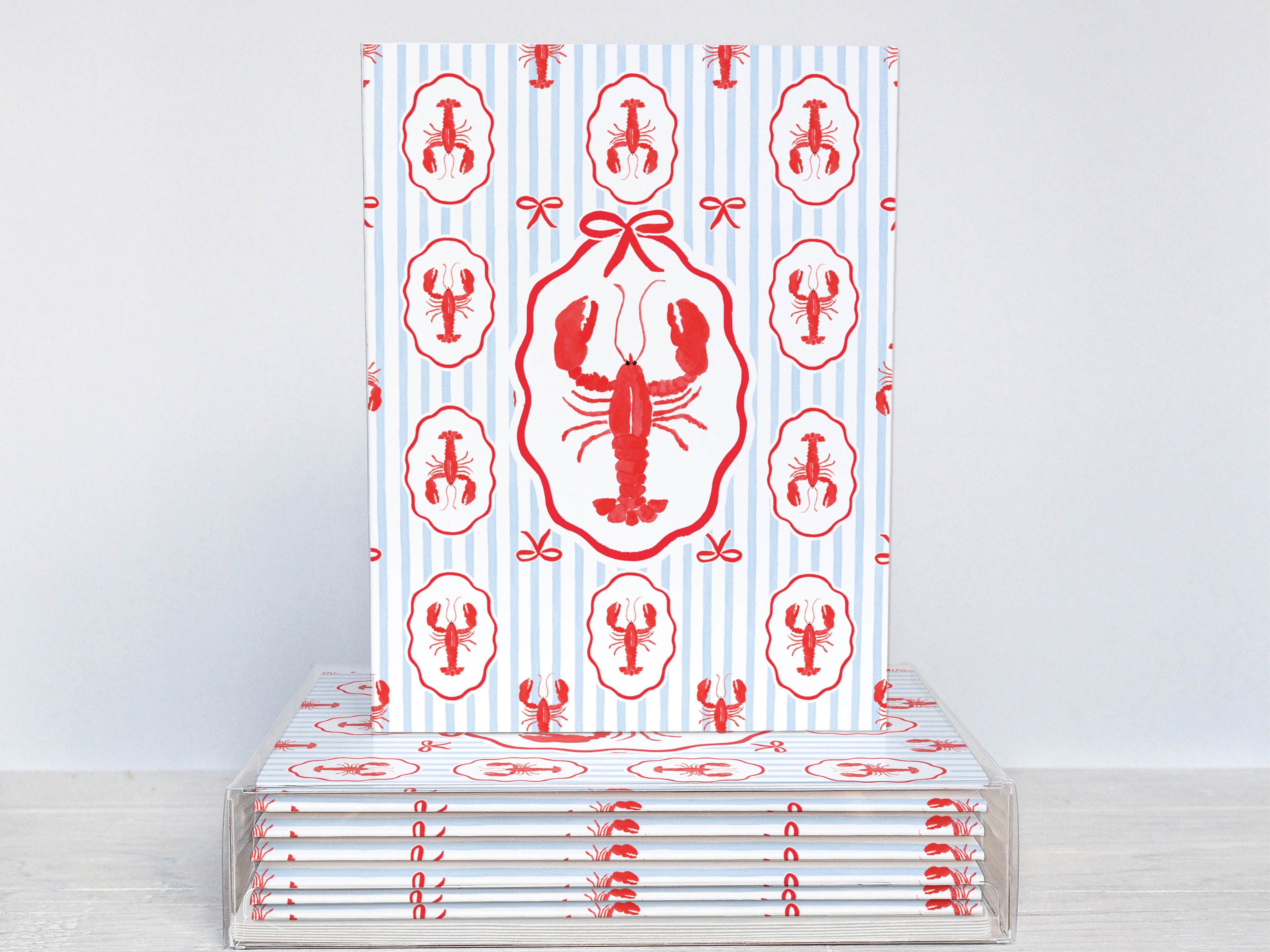 A stack of white notebooks with red lobster designs printed on them, placed on a white surface.