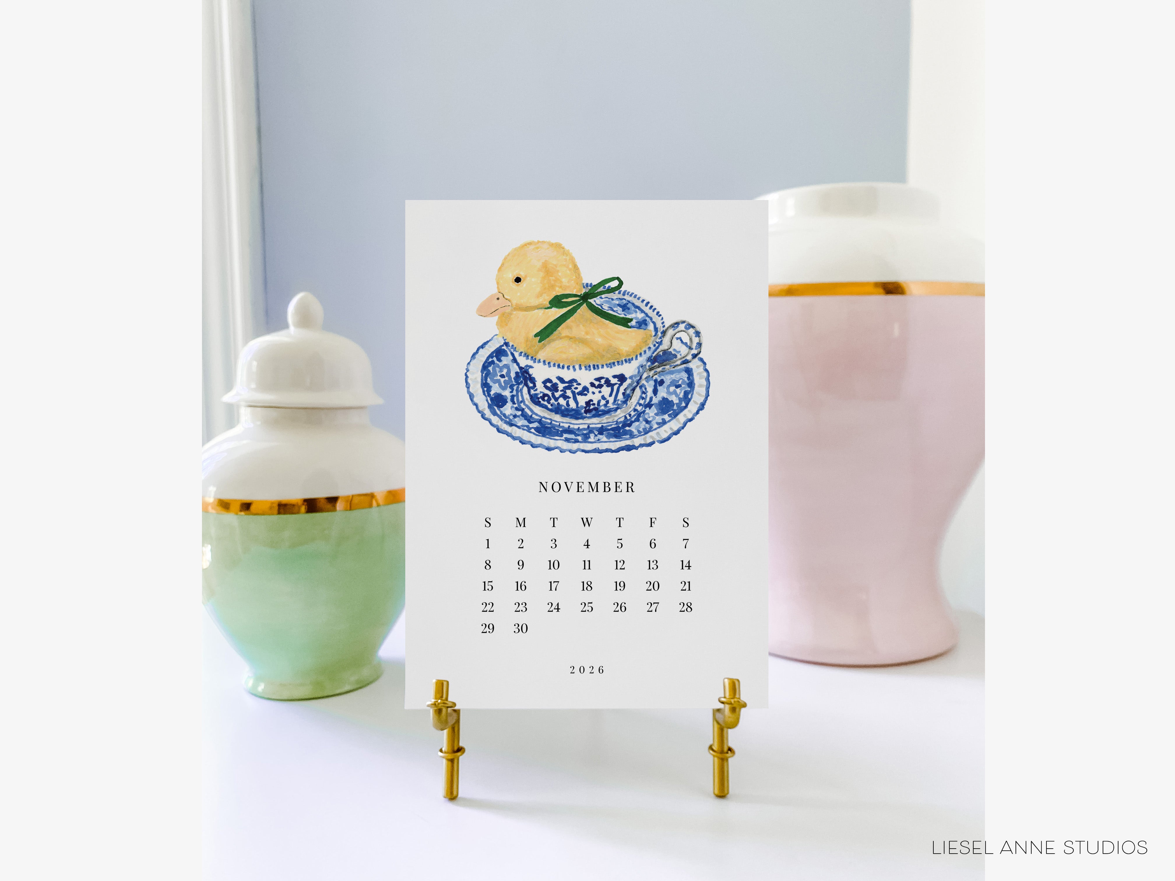 A calendar for November 2020 with a duck illustration on it, placed on a stand between two decorative vases.