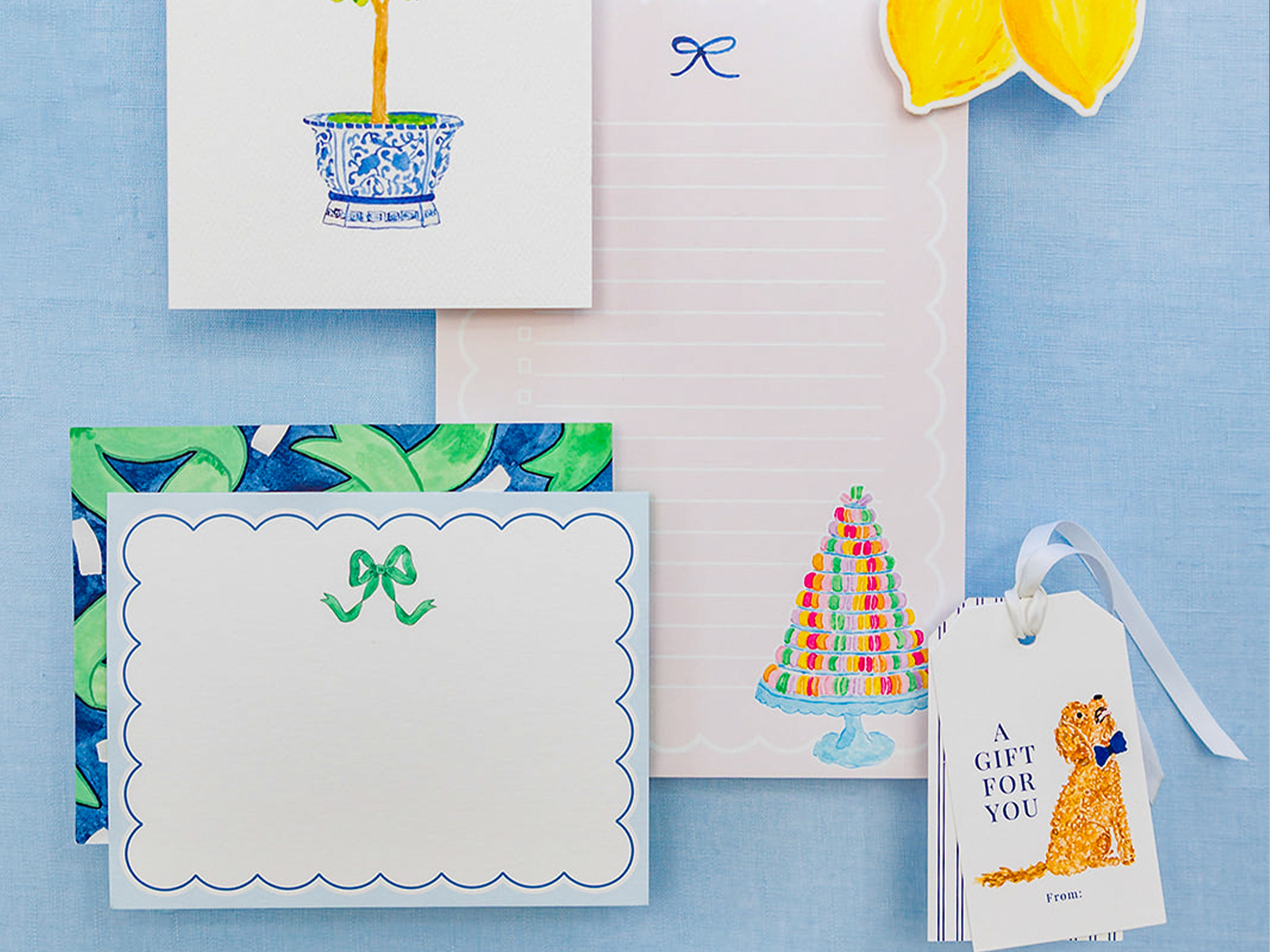 various decorative elements, including a blue and white ceramic pot, a green and white floral pattern, a white card with a bow, a white piece of paper with a tree illustration, and a tag with a dog illustration.