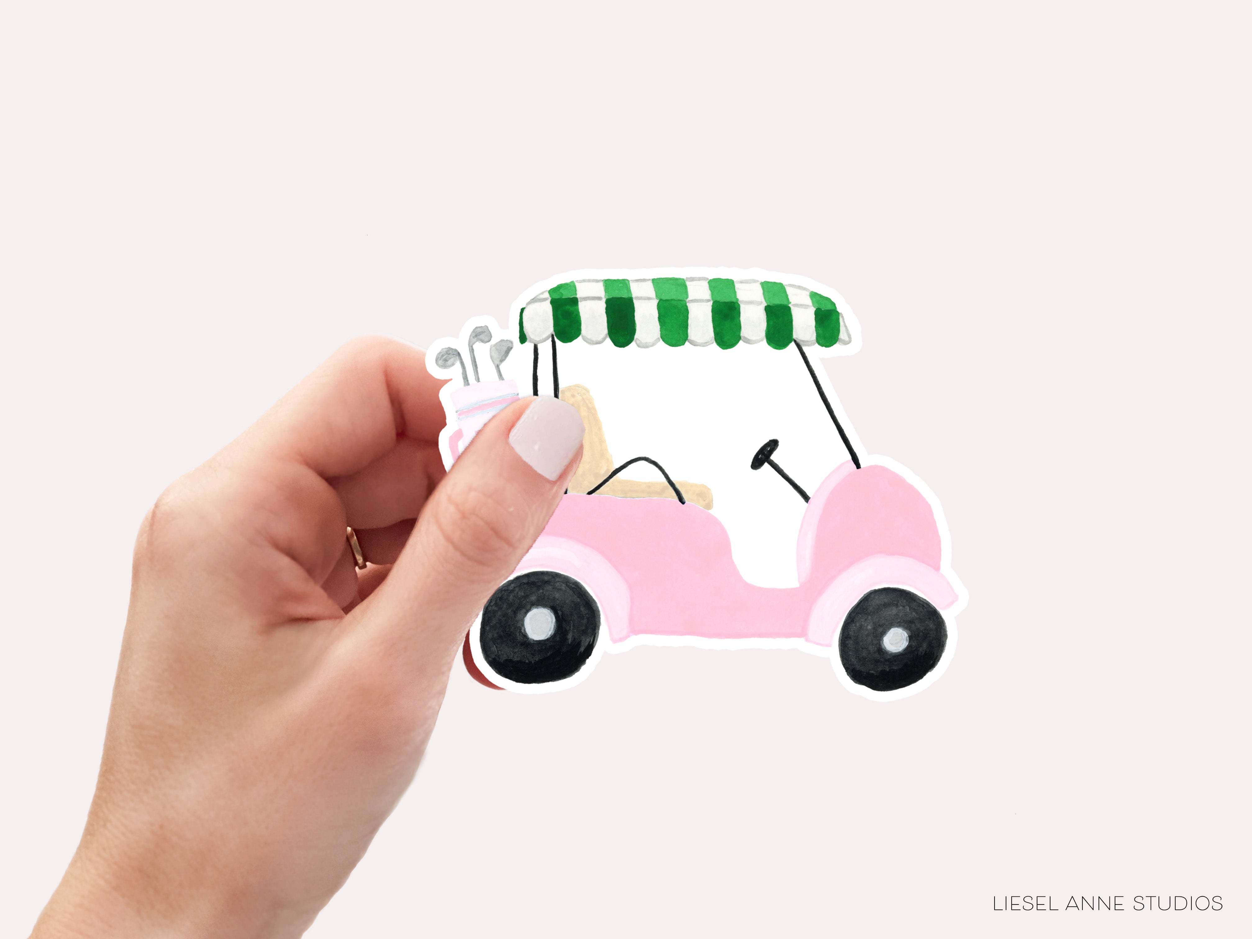 A hand holding a pink golf cart sticker against a white background.