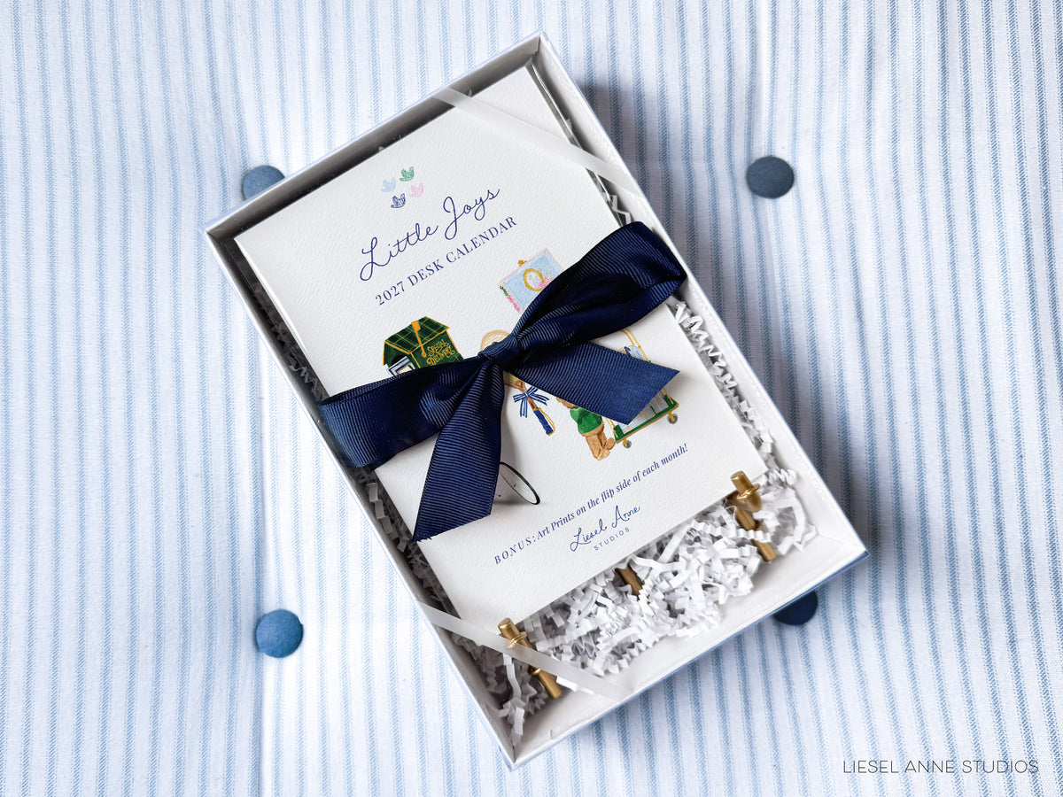 A white box with a blue ribbon and a white paper inside, placed on a striped fabric background.